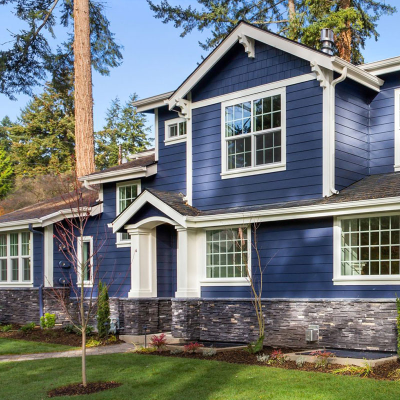 Blue custom home with white highlights and stone veneer with a green lawn.