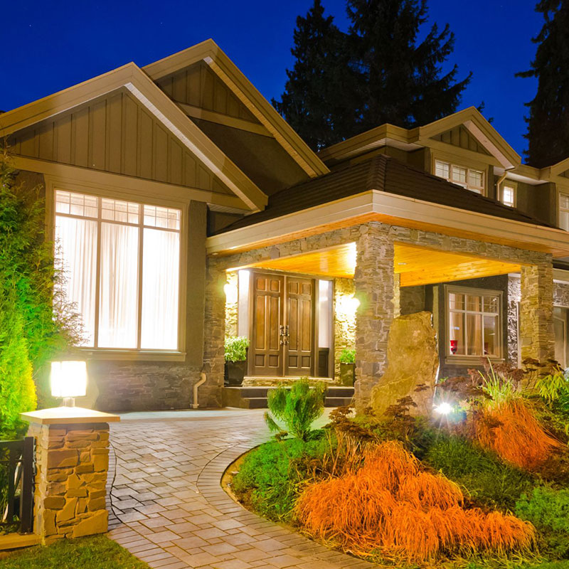 Custom home with stone columns and stone driveway lit up in the evening.